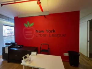Grรกfico de vinilo interior con el logo de New York Urban League en pared roja, รกrea de recepciรณn en Manhattan, NY