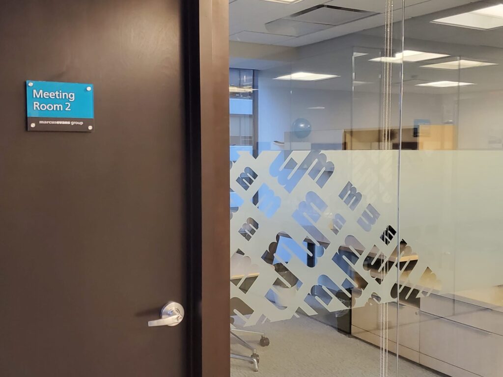 Office meeting room door with wall plaque sign and frosted glass graphic.